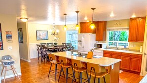 A spacious kitchen with wooden flooring, a central island with bar stools, pendant lighting, and wooden cabinets.
