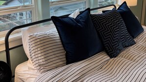 A bedroom with a bed, striped bedding, and a view of a residential area through large windows.