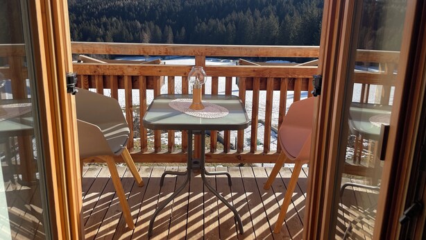 Une terrasse en bois avec deux chaises et une table, offrant une vue sur un paysage enneigé et des montagnes boisées.