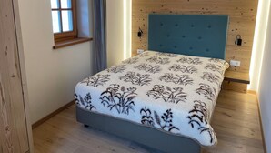 Une chambre avec une tête de lit en bois, une fenêtre avec un cadre en bois et un lit recouvert d’une couverture à motifs floraux.