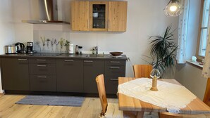 Une cuisine moderne avec des meubles de couleur sombre, une hotte de cuisine en acier inoxydable et une table à manger en bois recouverte d’une nappe blanche.