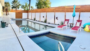 Una piscina con recinzione in legno, sdraio e un tavolino.
