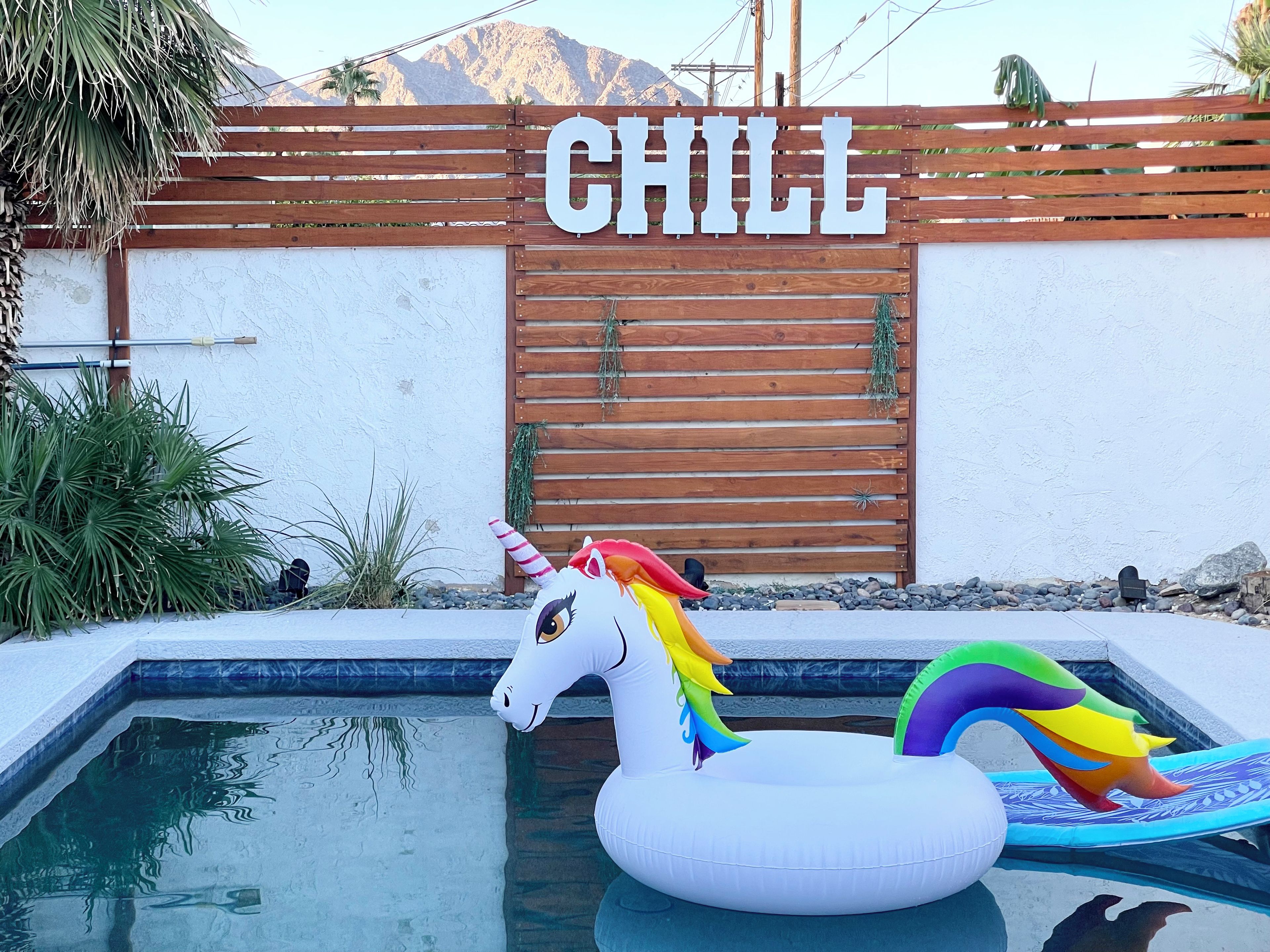 A pool area with a wooden fence, a sign that reads 'CHILL', and a unicorn float.