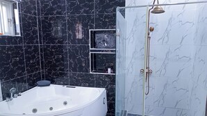 A modern bathroom with a large white bathtub, a glass-enclosed shower, and black marble tiles. - Luxury studio with Jacuzzi in a serene REstate (Lekki)
