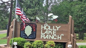A wooden sign for Holly Lake Ranch with an American flag and holly decorations. - Our Happy Place is located in the gated community of Holly Lake Ranch. (Hawkins)
