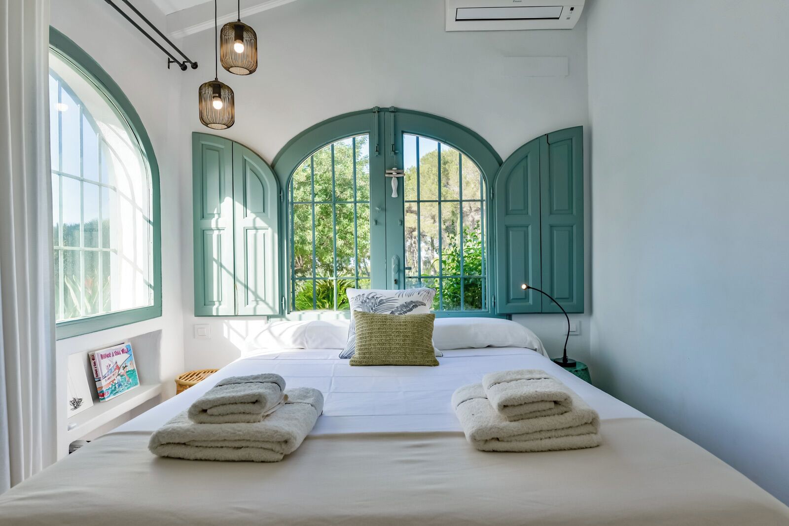 A bedroom with a bed, two windows with green shutters, a bedside lamp, and a framed picture on the wall.