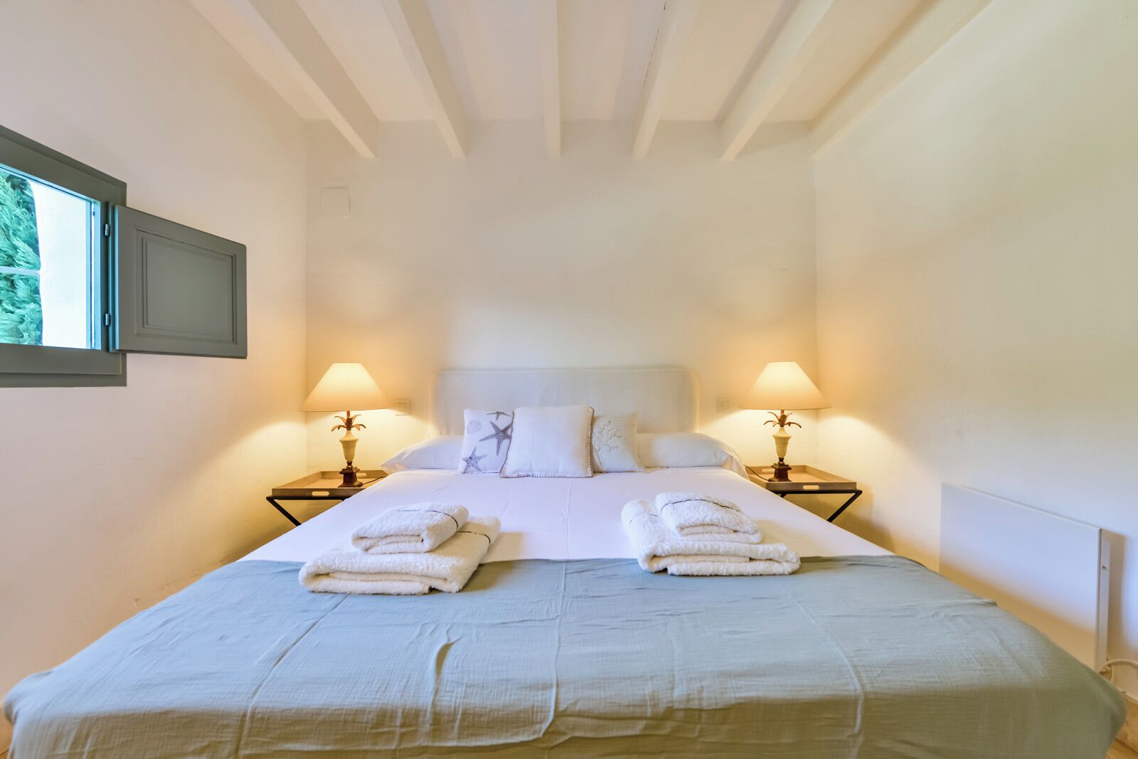 A neatly made bed with two pillows, two bedside lamps, and two folded towels on the bed.