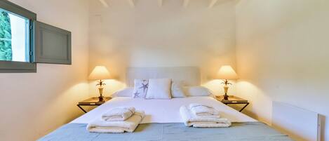 A neatly made bed with two pillows, two bedside lamps, and two folded towels on the bed.