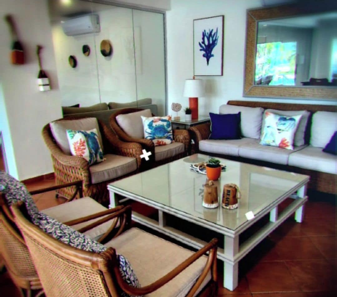 A living room with wicker furniture, a glass coffee table, and a large mirror.