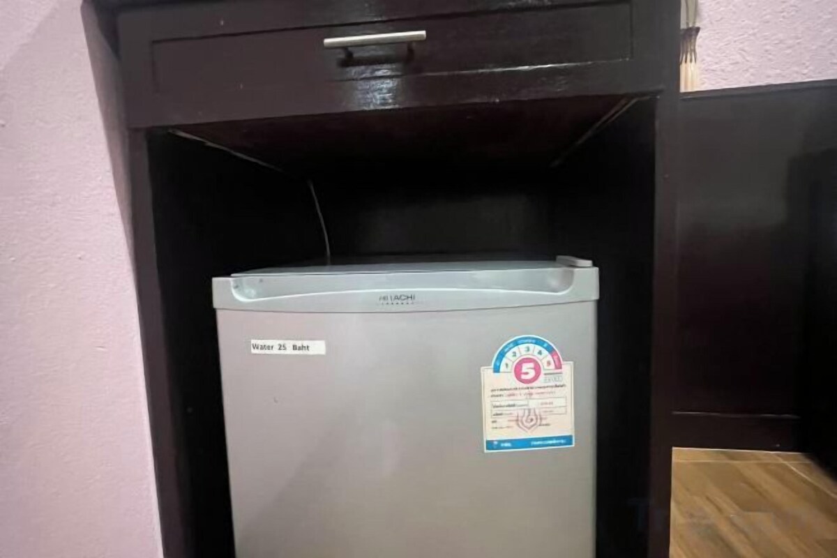 Un refrigerador compacto con dispensador de agua y hielo, ubicado debajo de un mueble oscuro.