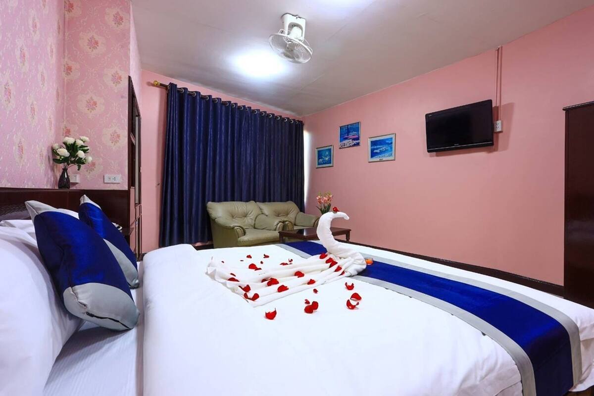 Une chambre d’hôtel avec deux lits, un téléviseur à écran plat, un ventilateur de plafond et un papier peint à motifs floraux.