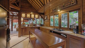 A spacious kitchen with wooden beams, a long counter, and a refrigerator. - Sungai Villa by Betterplace (Canggu)