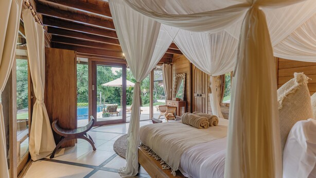 A bedroom with a canopy bed, wooden flooring, and a view of the outdoors. - Sungai Villa by Betterplace (Canggu)