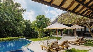 A poolside area with a clear blue pool, wooden lounge chairs, and umbrellas. - Sungai Villa by Betterplace (Canggu)