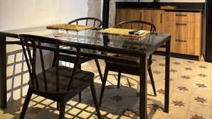A dining area with a glass table, chairs, a kitchen with wooden cabinets, and a built-in stove.
