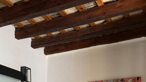 A bedroom with a bed, a painting, a wall-mounted light, and a wooden ceiling.