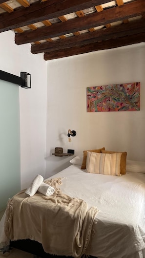 Un dormitorio con cama, un cuadro, una lámpara en la pared y techo de madera.