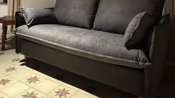 A sofa in a room with a tiled floor, wooden ceiling beams, and curtains.