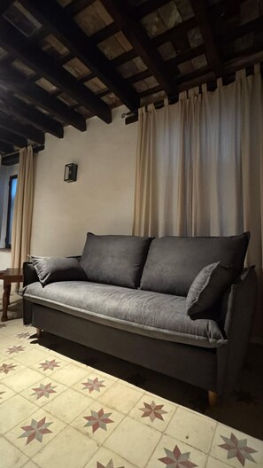 Ein Sofa in einem Raum mit Fliesenboden, Holzbalkendecke und Vorhängen.