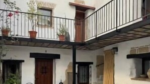 A courtyard with a checkered floor, potted plants, a wooden bench, and a balcony.