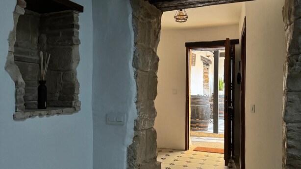 A narrow hallway with stone walls, a tiled floor, and a doorway leading to an outdoor area.