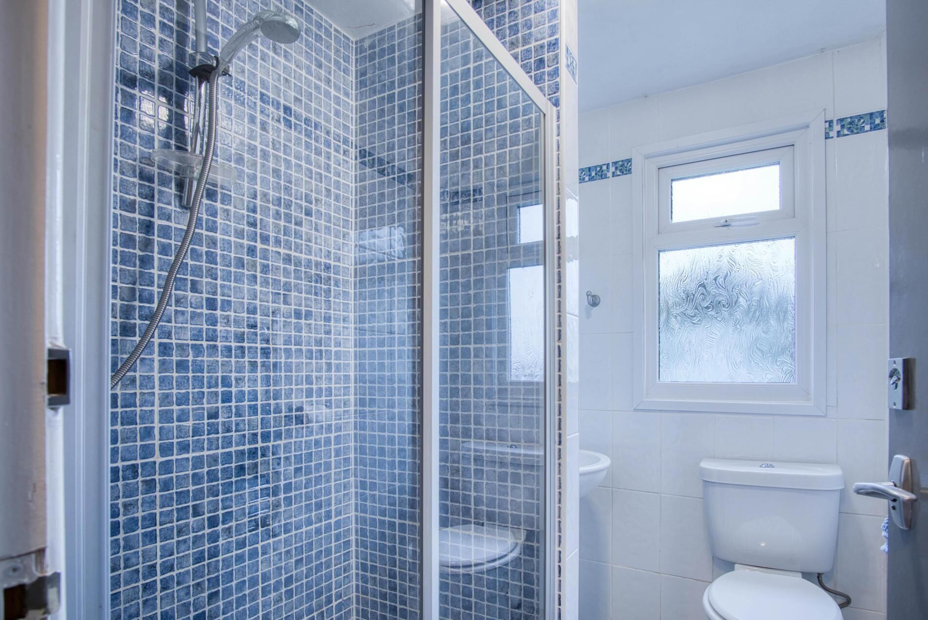 Et badeværelse med glasbrusekabine, toilet og et vindue.