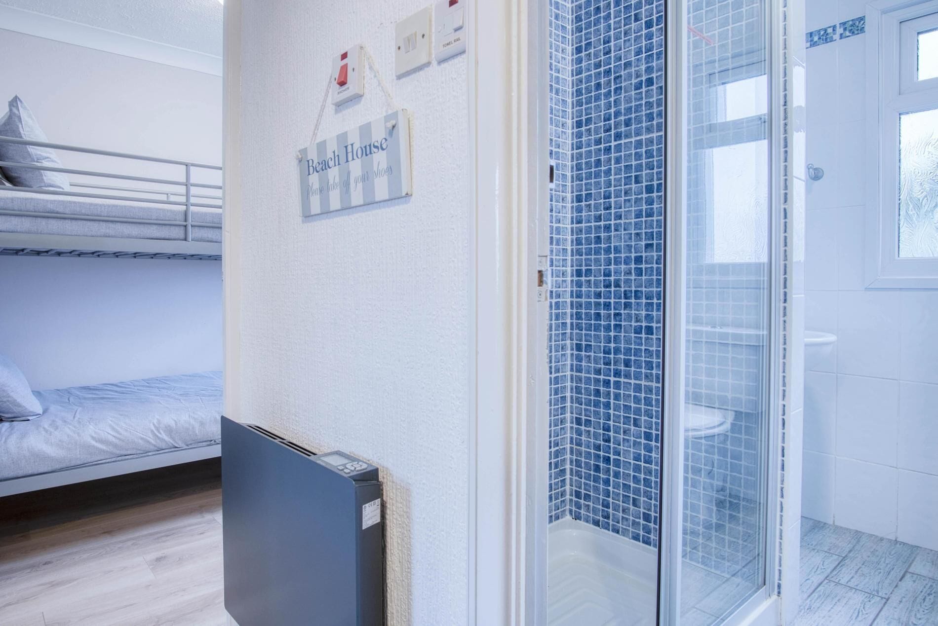 A hotel room with a bunk bed, a shower with blue mosaic tiles, and a sign that says "Beach House".