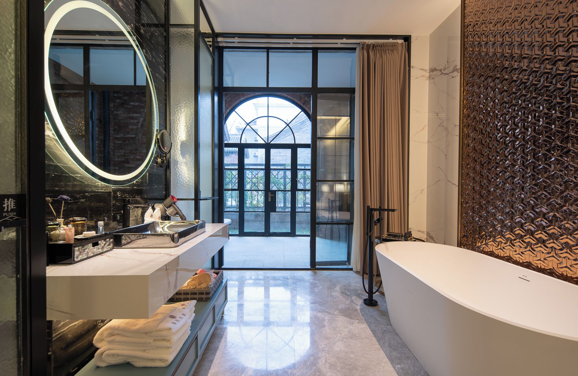 A modern bathroom with a large mirror, a vanity with a sink, a bathtub, and a view through a large window.