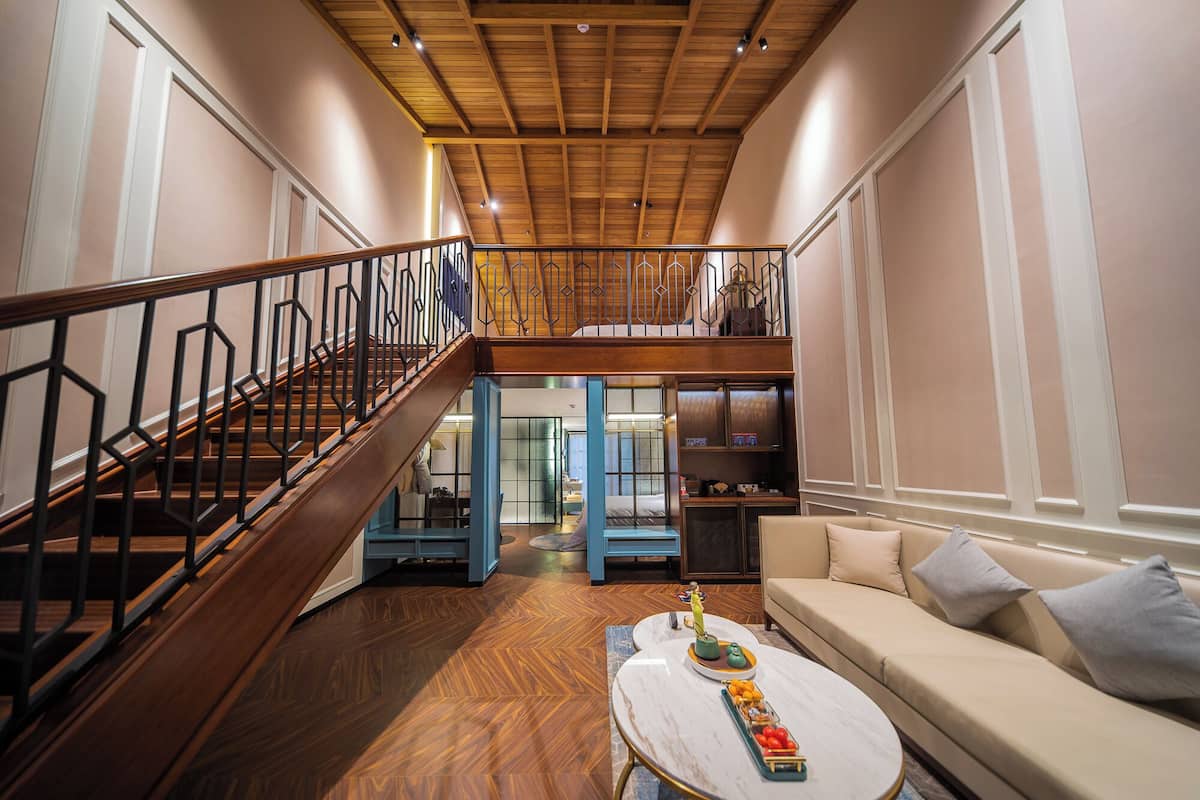 A spacious living area with a wooden staircase, a sofa, a coffee table, and a view of the upper floor.