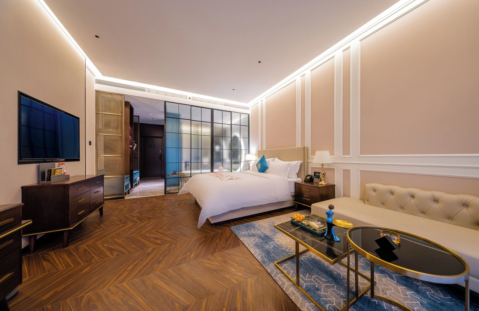 A hotel room with a large bed, a sofa, a TV, a desk, and a mirror.