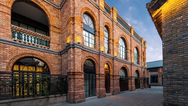 A historic building with arched windows and brickwork, featuring a courtyard and a gated entrance. - SECLUSION TANG (Luoyang)