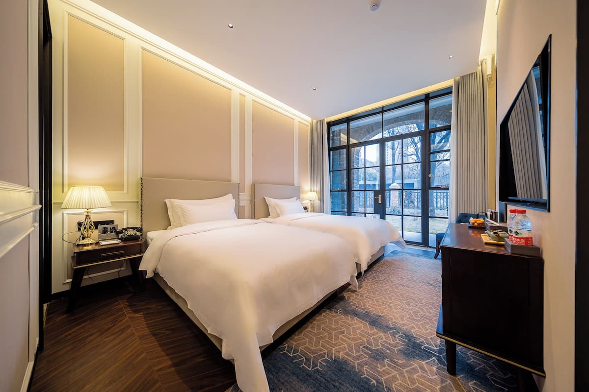 A hotel room with a large bed, a desk, a chair, a TV, and a window with a view of trees.