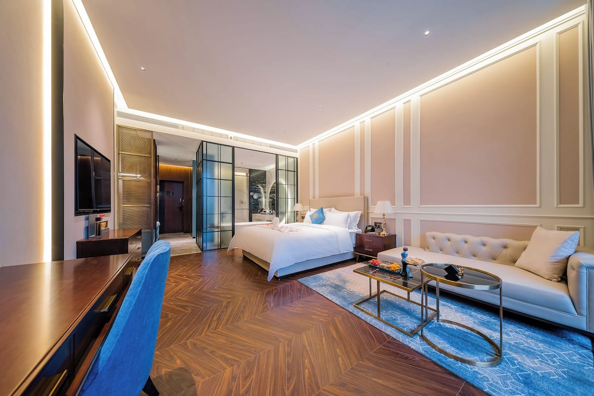A modern hotel room with a large bed, a sofa, a TV, and a desk.