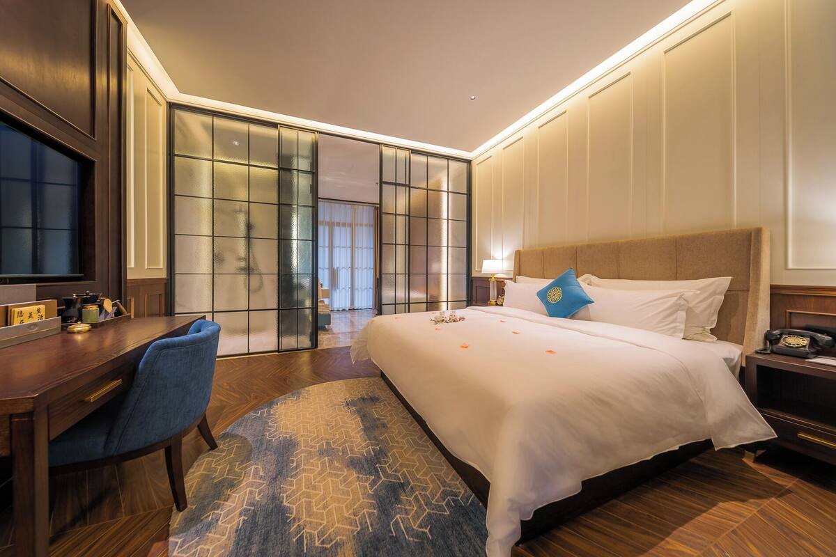 A hotel room with a large bed, a desk, a chair, and a television.