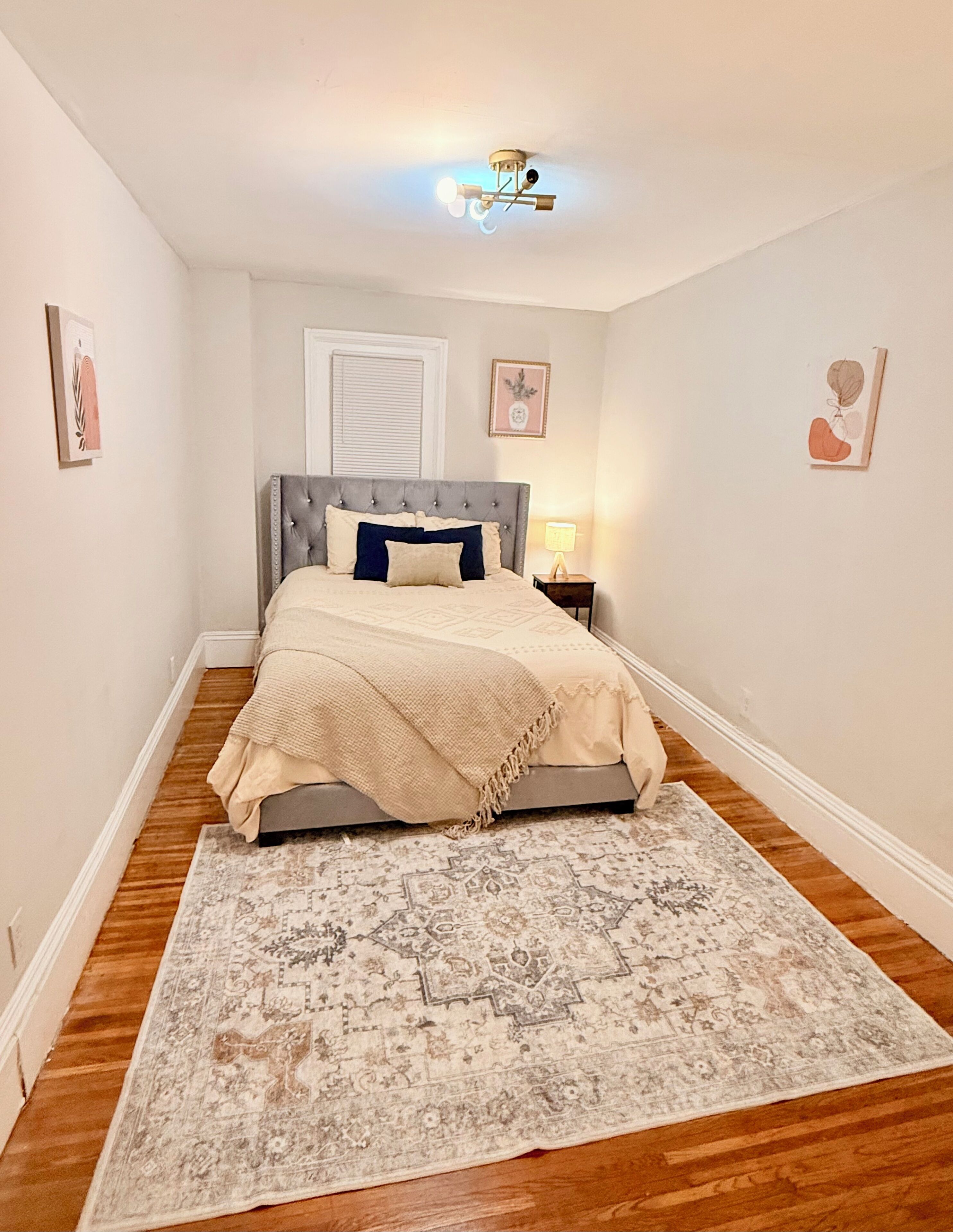 A bedroom with a bed, a nightstand, a ceiling fan, and a patterned rug.