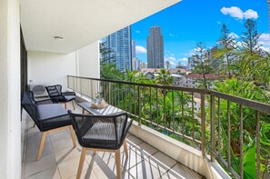 Varanda com mesa e cadeiras, vista para um horizonte urbano com edifícios altos e áreas verdes.