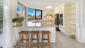 Una cocina moderna con una isla grande, taburetes de bar, electrodomésticos integrados y vistas al exterior.