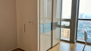 Ein Zimmer mit einer großen Schiebeglastür, die auf eine Stadtansicht führt, einem Flachbildfernseher auf einem Schrank und einem Holzboden.