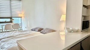 Ein modernes Hotelzimmer mit einem großen Bett, einem Schreibtisch mit Stühlen, einer Mikrowelle und einem Fenster mit Jalousien.