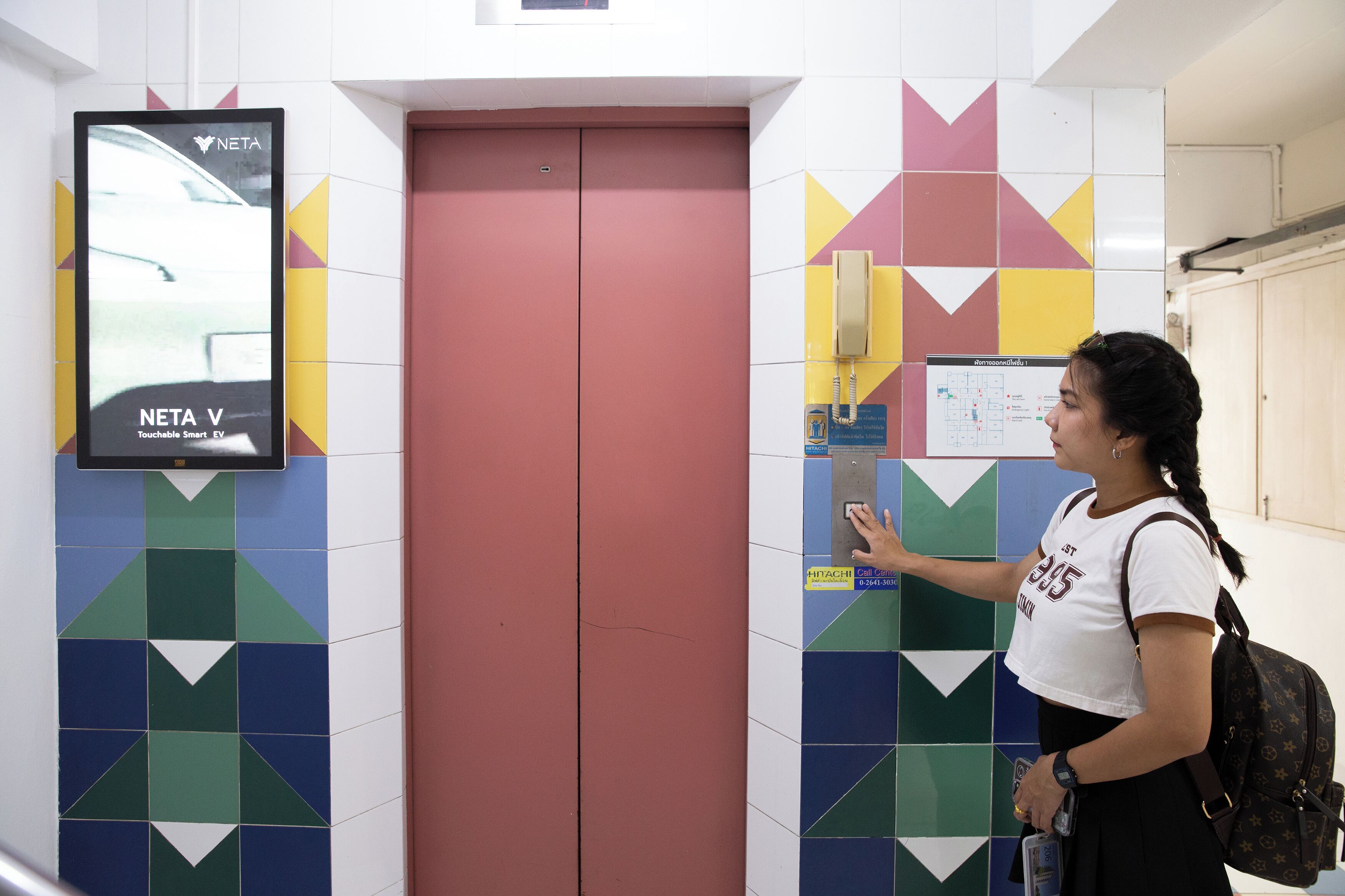 A woman using a touchscreen kiosk in an elevator with a colorful geometric tile wall.