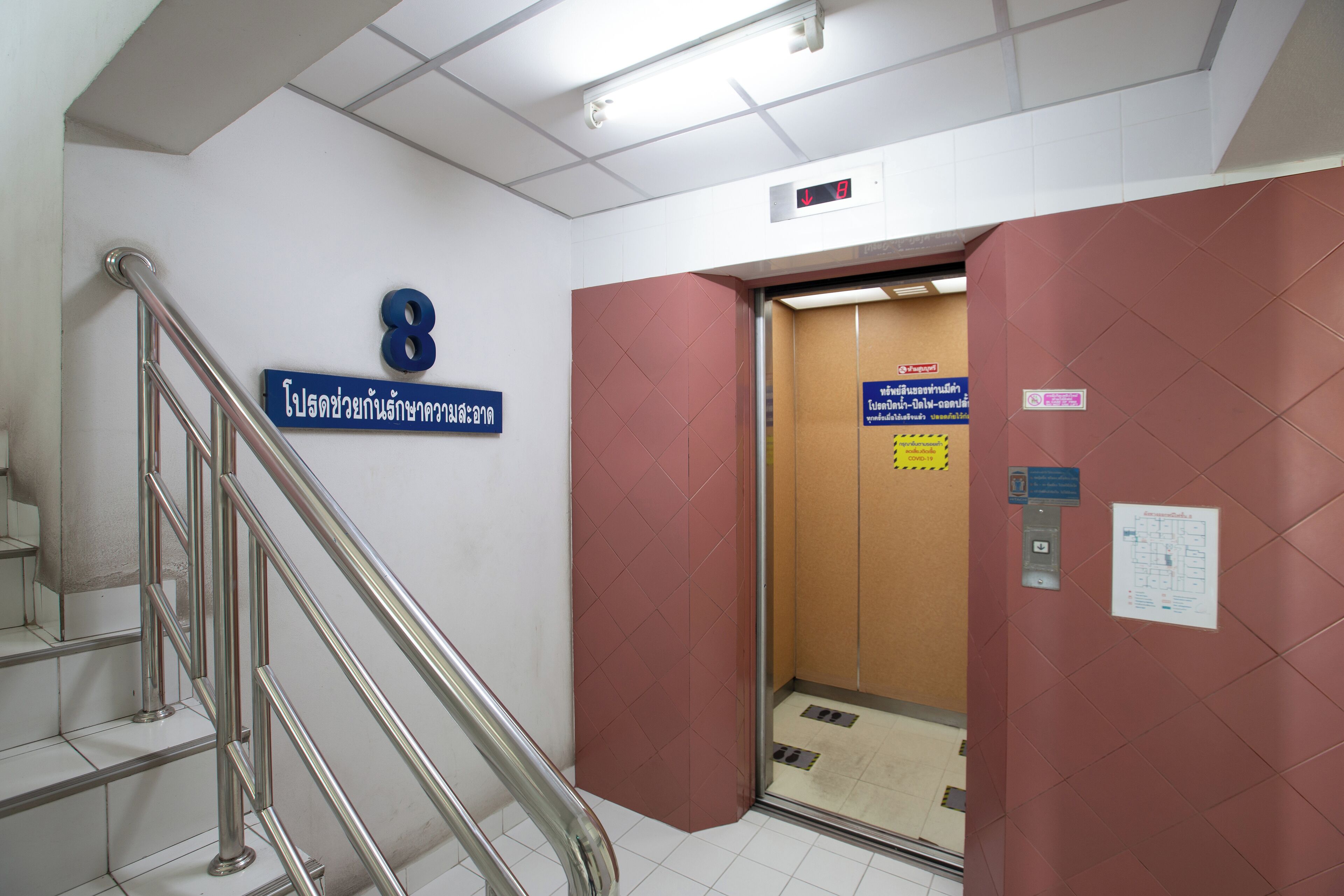 A stairwell with a metal handrail, a blue sign with the number 8, and a brown elevator door.