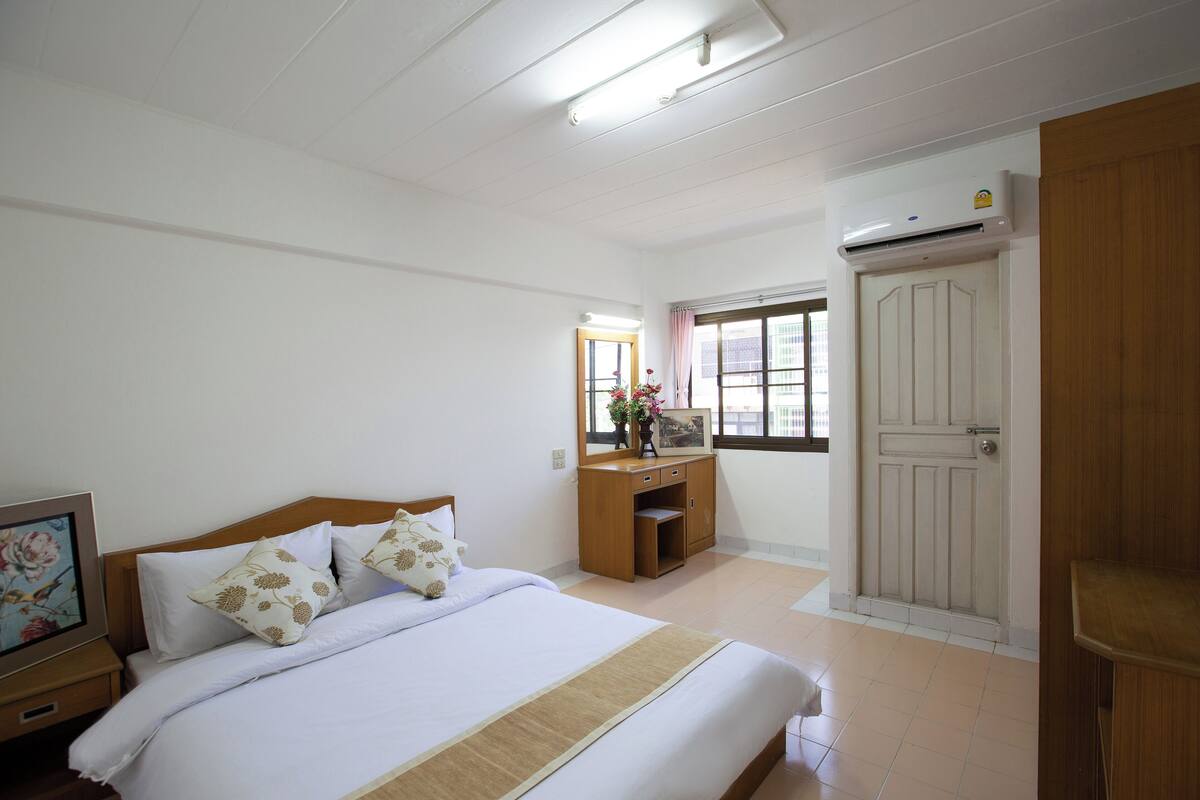 Une chambre d’hôtel avec un lit, une table de chevet en bois, un bureau et une armoire.