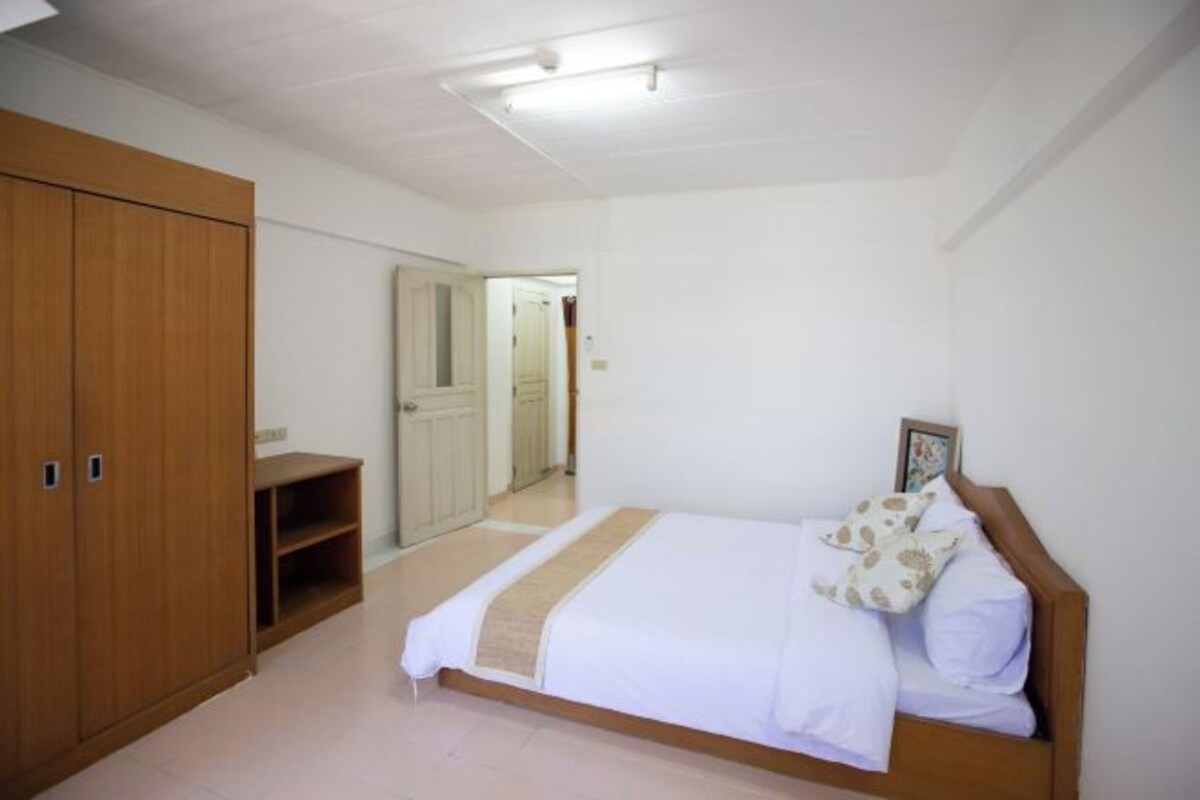 A bedroom with a bed, wooden wardrobe, and a door leading to another room.