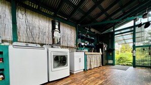 A laundry area with a washing machine and dryer, wooden flooring, and a view of greenery through a glass door.