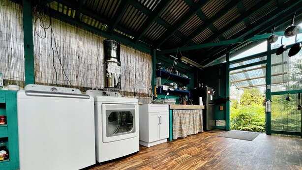 A laundry area with a washing machine and dryer, wooden flooring, and a view of greenery through a glass door.