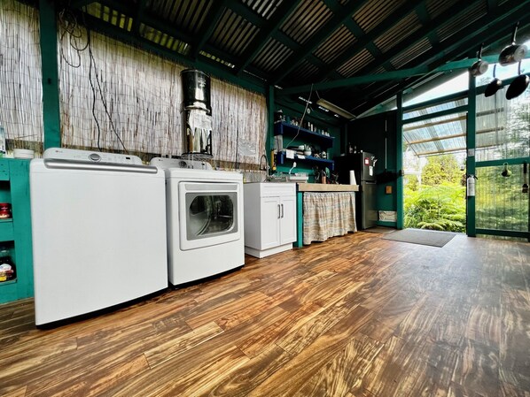 A laundry area with a washing machine and dryer, wooden flooring, and a view of greenery through a glass door.