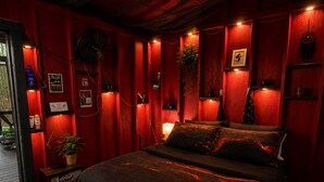 A room with a bed, a small table, a potted plant, and a wall-mounted shelf.