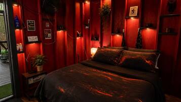 A room with a bed, a small table, a potted plant, and a wall-mounted shelf.