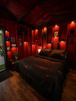 A room with a bed, a small table, a potted plant, and a wall-mounted shelf.