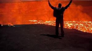 A person standing with arms raised in front of a lava flow.